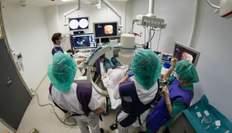 Undersøkelsesrom 113 er fullt av medisinsk teknologi.  12 ulike dataskjermer, tre leger, en ingeniør, en cytodiagnostiker og fire sykepleiere og en pasient må til under forsøkene med det nye bronkoskopet og navigasjonssystemet. Undersøkelsen ledes av lungelege Tor Amundsen, mens lege Hanne Sorger står "ved spakene". Foto: Thor Nielsen.