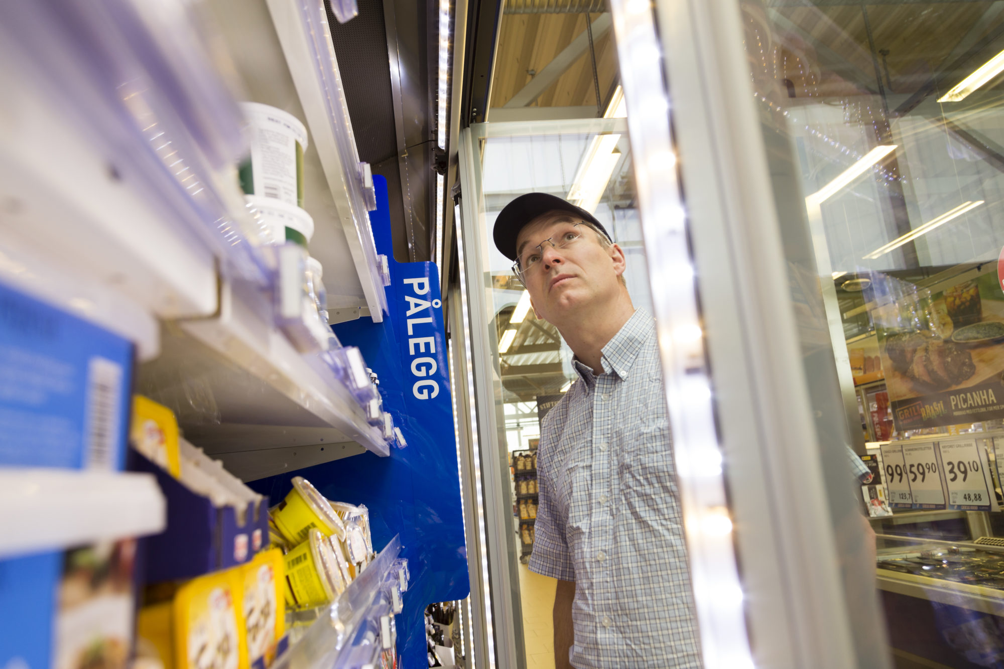 Mann med med blå skjermlue/caps ser inn i kjøledisk på Rema-butikk