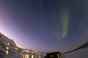 Ny-Ålesund på sitt lyseste i januar – solen er fortsatt under horisonten, men lyser opp himmelen i sør. Samtidig danser nordlyset godt synlig midt på himmelen. Foto: Geir Johnsen, NTNU.