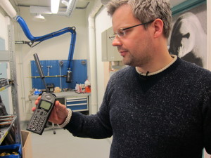 Martin Indreiten, koordinator for logistikk ved UNIS, viser frem en satellittelefon som studenter og forskere bruker når det er nødvendig. Bak ham ser du en isbjørnplakat som blir brukt til skytetrening. Foto: Nancy Bazilchuk/NTNU