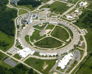Luftfoto av sirkelformet laborium omgitt av grønt gress. Anlegget inneholder en slags racerbane for elektroner., men denne er skjult på bildet, under anleggets tak.