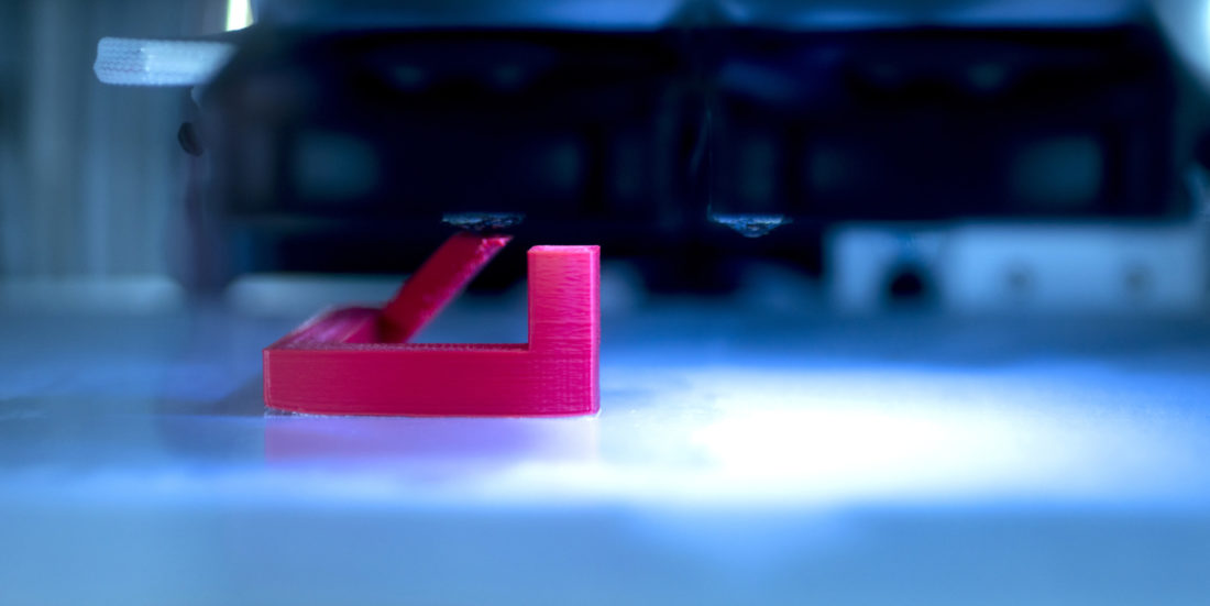Rød plastfigur blir til i laserlys i 3D-printing