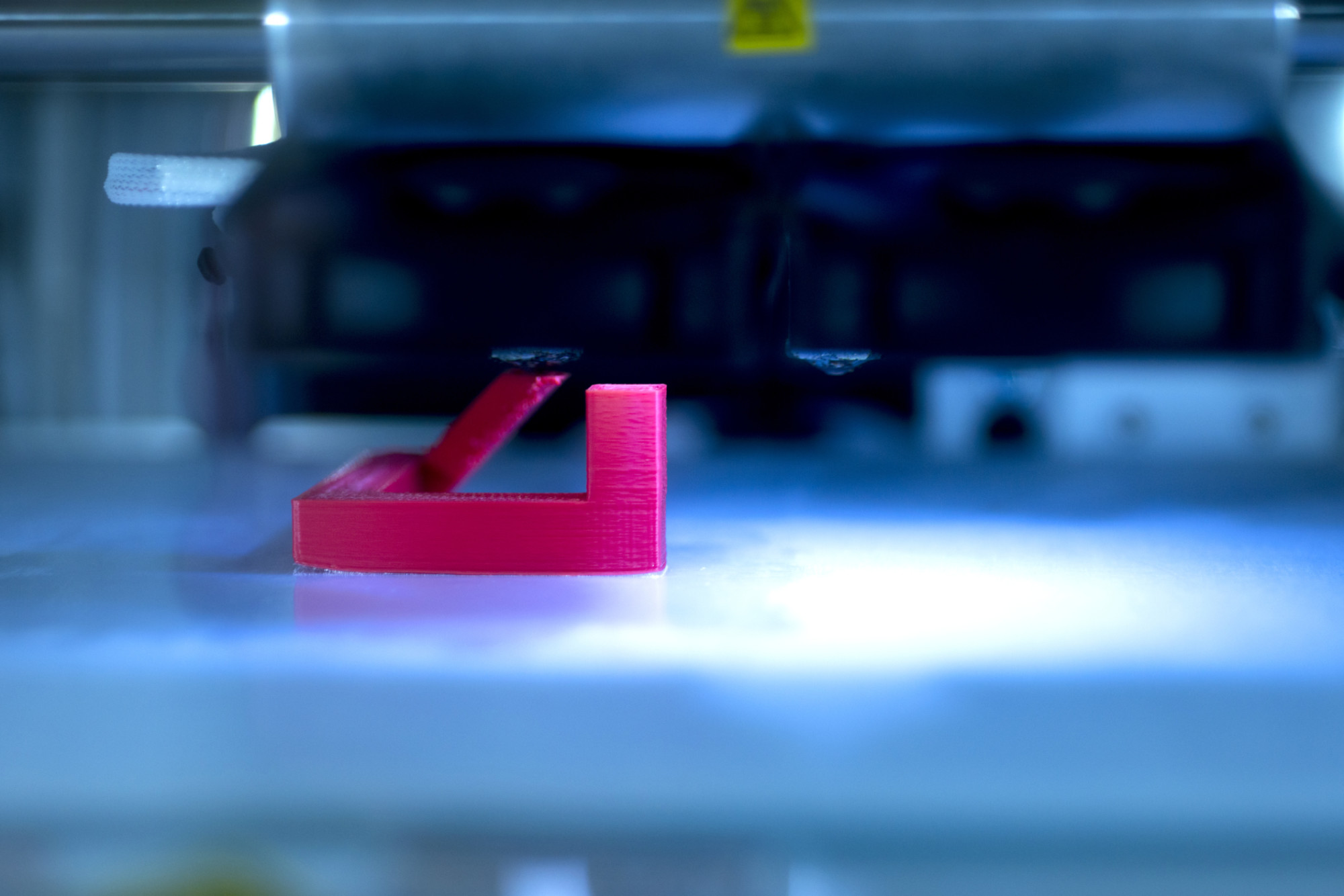 Rød plastfigur blir til i laserlys i 3D-printing