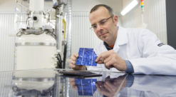 Mann i hvit frakk sitter på laboratorium der han ser på solcelle han holder i hendene.