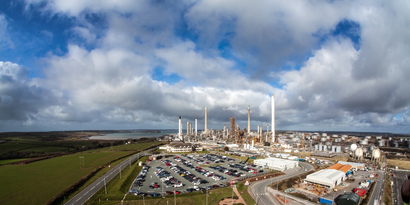 Fabrikkpiper fotografert på avstad, hvit damp blander seg med hvite skyer på blå himmel
