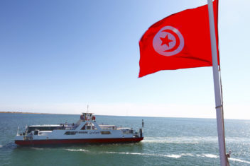 Ferge på blått hav. I forgrunnen ses flagget til Tunisia - rødt, med hvit sirkel, og inni sirkelen en stjerne og en halvmåne