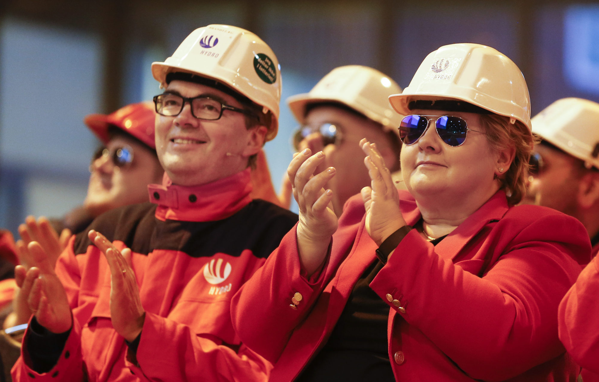 Gruppe mennesker med oransje og røde jakker og hvit hjelm på hodet, applauderer. en av dem er statsminiser Erna Solberg.