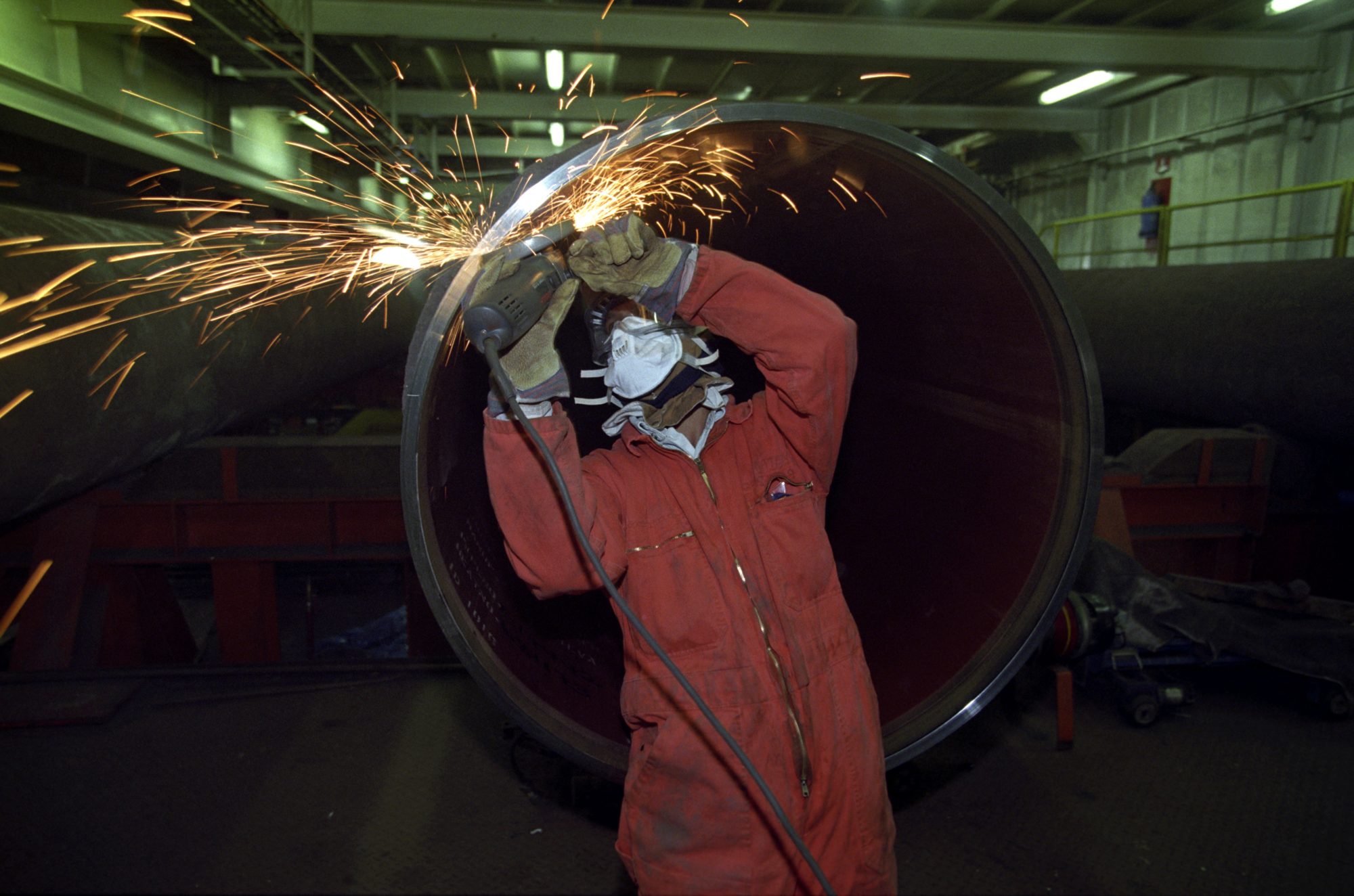 Industriarbeider fotografert i det han/hun driver sveisearbeid ved tverrenden av stort stålrør.