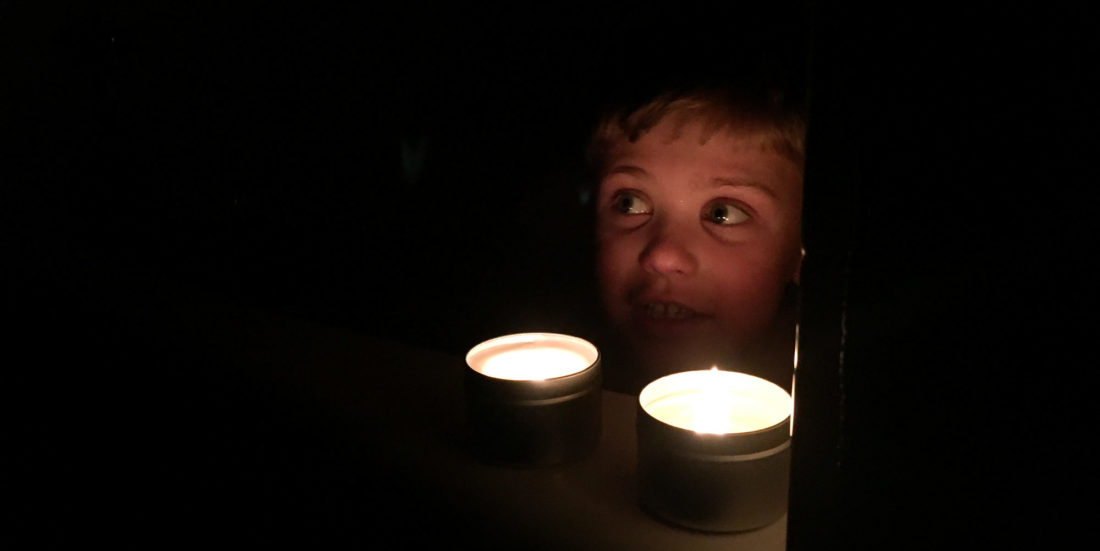 Liten gutt sitter i mørket, foran to fakkelbokser, åpenbart etter at strømmen har gått