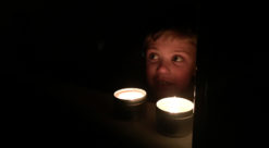 Liten gutt sitter i mørket, foran to fakkelbokser, åpenbart etter at strømmen har gått