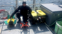 Foto.Mann i dykkerdrakt med en skilpadderobot på båtdekk.