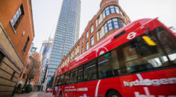 Rød dobbeltdekker buss med hvit påskrift "hydrogen bus" kjører gjennom London-gata med høyhus i bakgrunnen