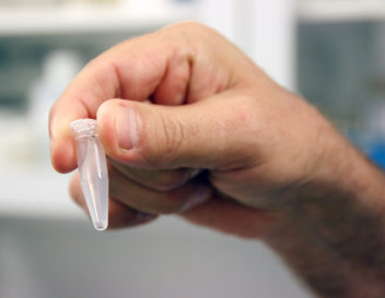 Hånd som holder i en liten plastbeholder med koronatest.
