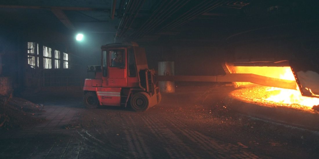 Bilde fra mørk smelteverkshall der oransje spesialtruck "staker" i ildmørja i en smelteovn.