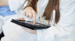 Kvinne i hvit helseuniform holder laptop i fanget
