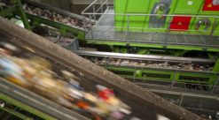Grønn sorteringsmaskin sorterer plast som fyker forbi på transportbånd i forgrunnen.