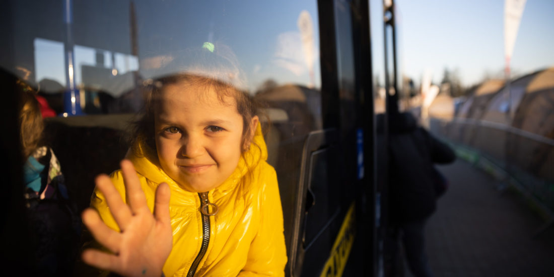 Liten jente som har flyktet fra Ukraina , vinker ut gjennom bussvindu.