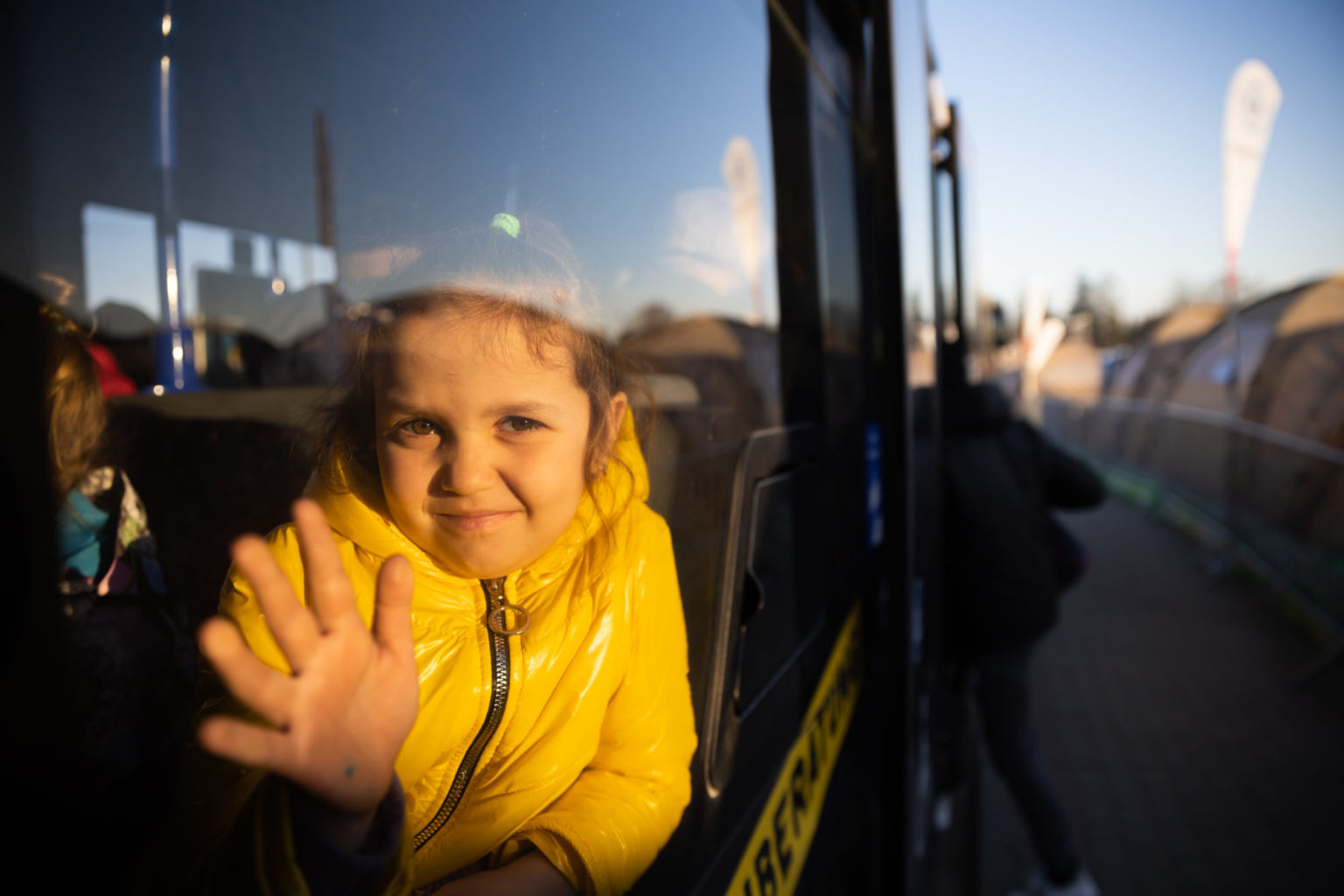 Liten jente som har flyktet fra Ukraina , vinker ut gjennom bussvindu.
