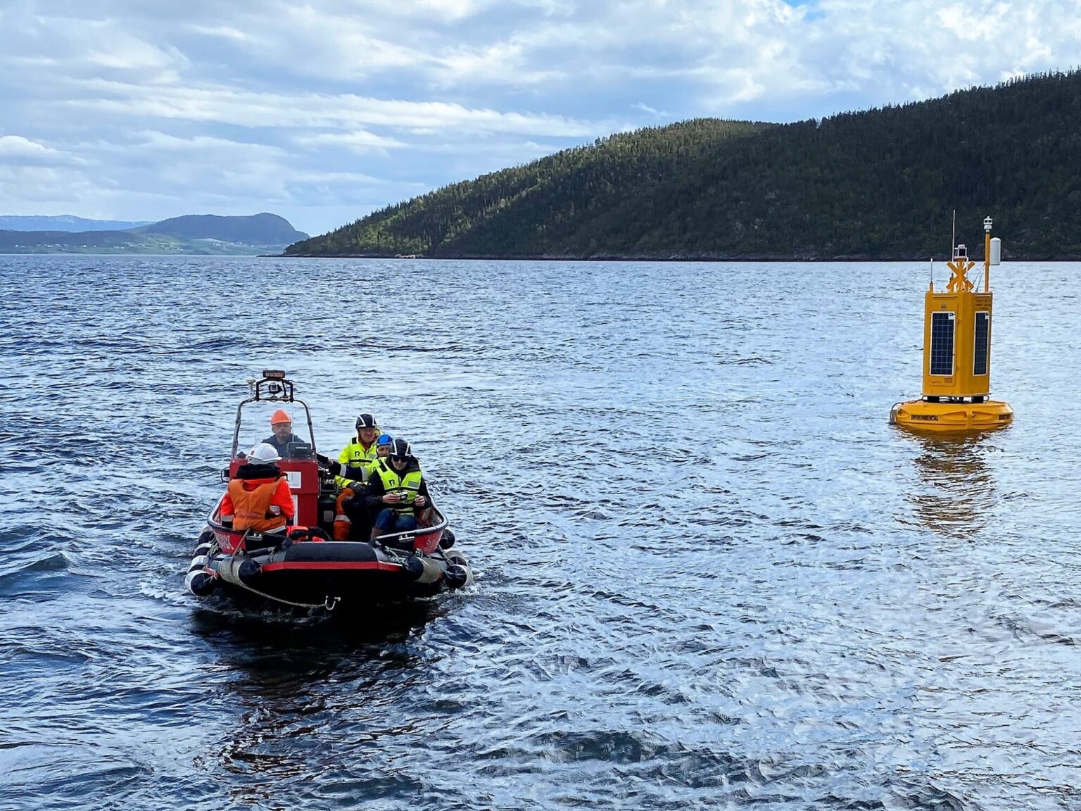 Fire-fem mennesker i svart gummibåt kjører bort fra gul flytende observasjonsbøye i Trondheimsfjorden.