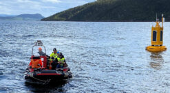 Fire-fem mennesker i svart gummibåt kjører bort fra gul flytende observasjonsbøye i Trondheimsfjorden.