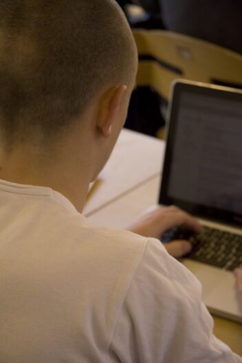 Bildet viser en ung mann ved en datamaskin. Fotografert bakfra.