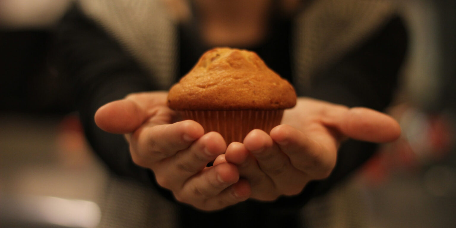 Hender som holder fram en muffins