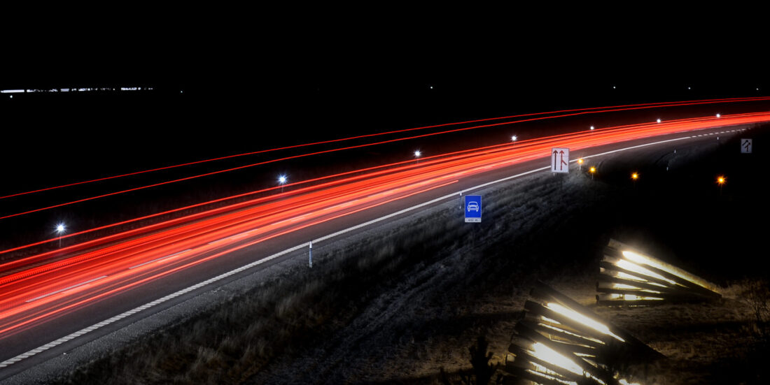 Nattbilde av motorvei, tatt med lang eksponeringstid. Lysene fra biltrafikken vises dermed som et rødt "bånd" mot de svarte omgivelsene.