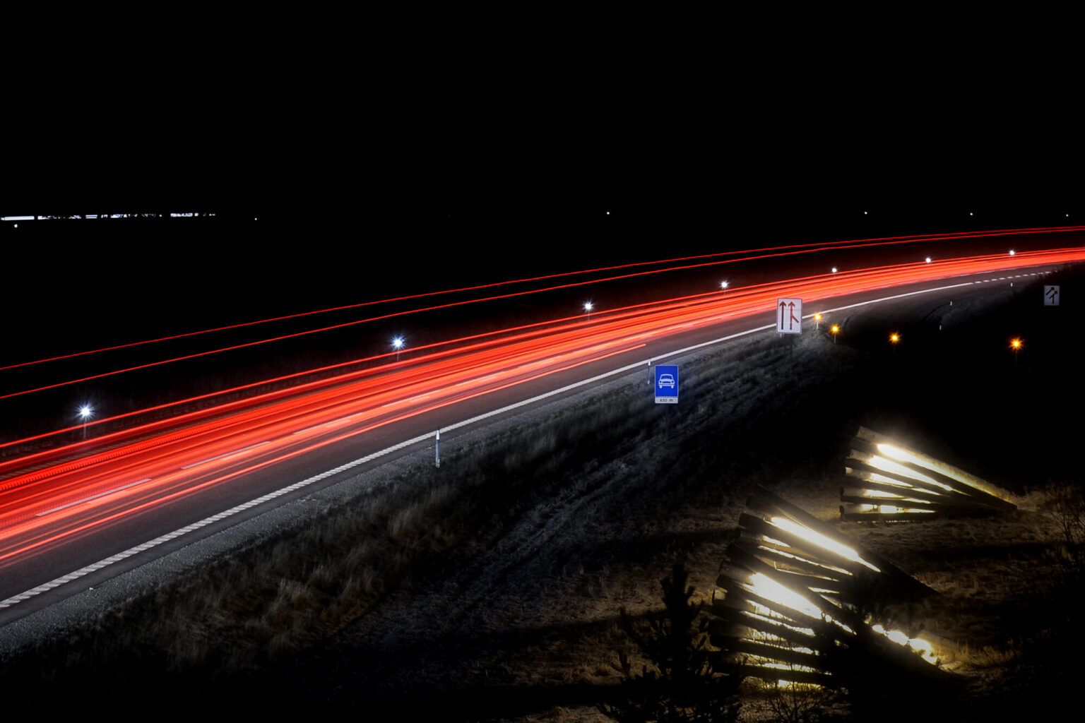 Nattbilde av motorvei, tatt med lang eksponeringstid. Lysene fra biltrafikken vises dermed som et rødt "bånd" mot de svarte omgivelsene.