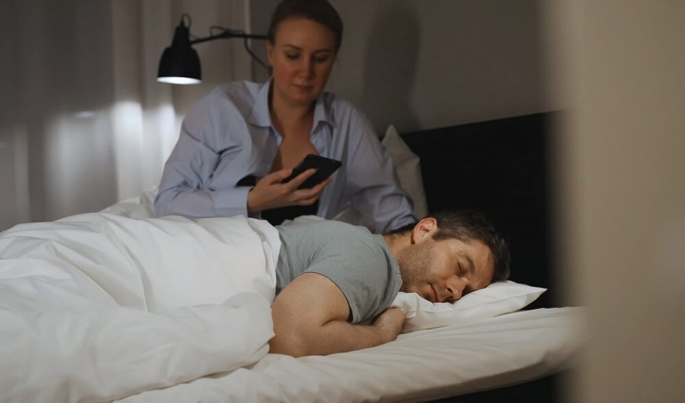 Dobbeltstandard. Kvinne sjekker partnerens telefon i senga.