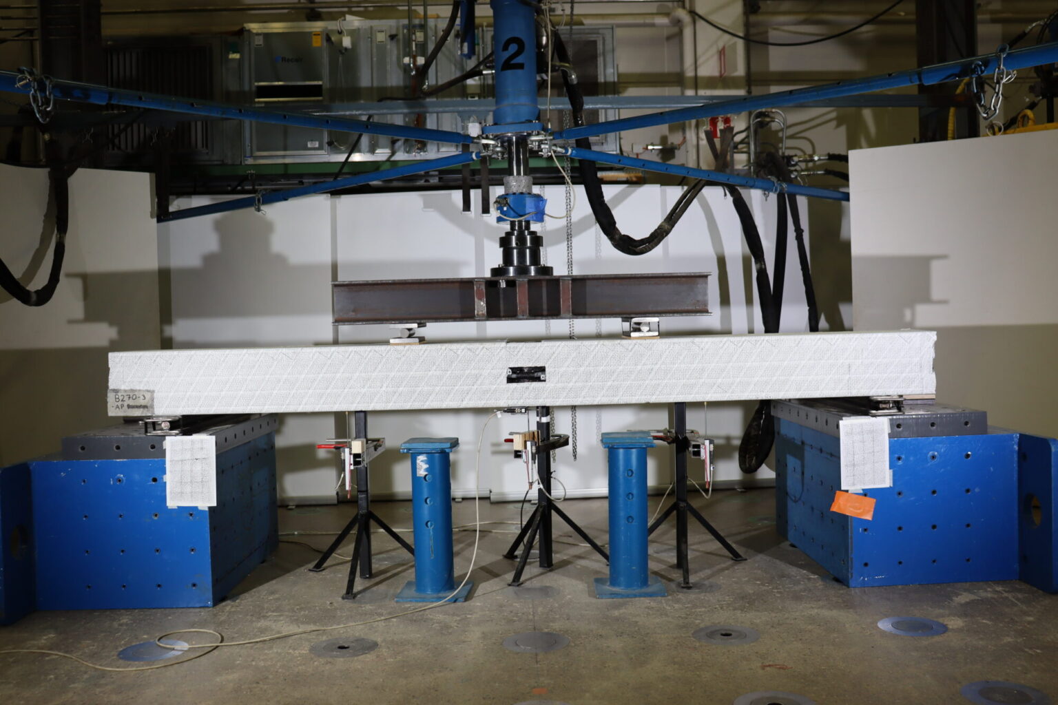 Bildet viser en betongpæle som gjennomgår en bøyetest i en mekanisk lab.