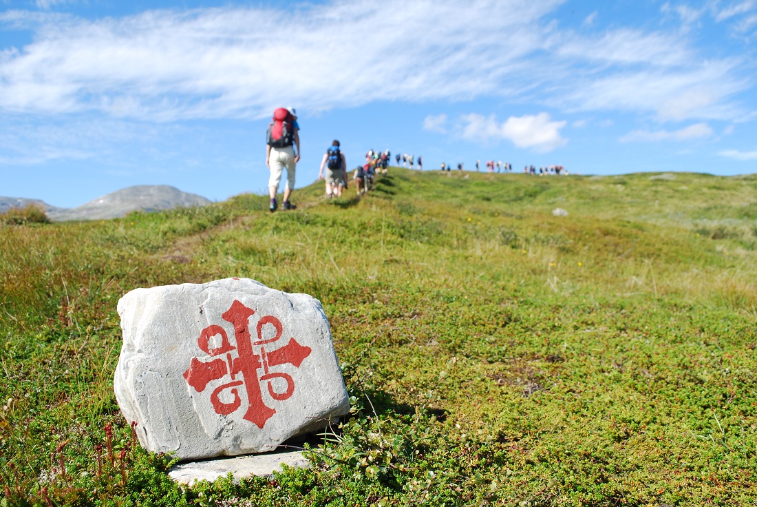 Bildet viser en stein i fjellheimen med merket for pilegrimsleden.