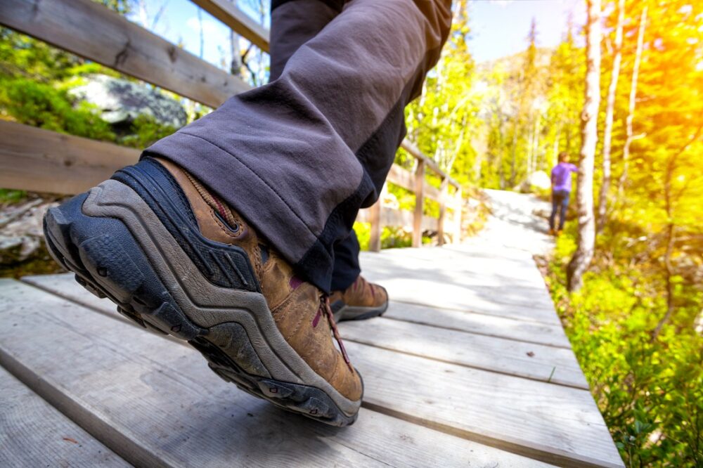 Medisiner. Nærbilde av føttene til en vandrer på en tursti belagt med planker.