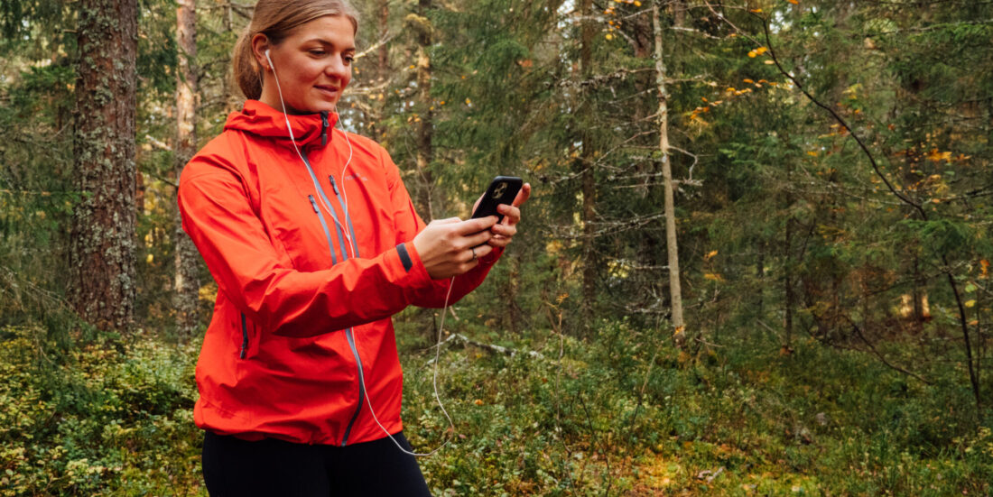 Spill. Kvinne som løper i skogen med Myworkout-app på telefonen.