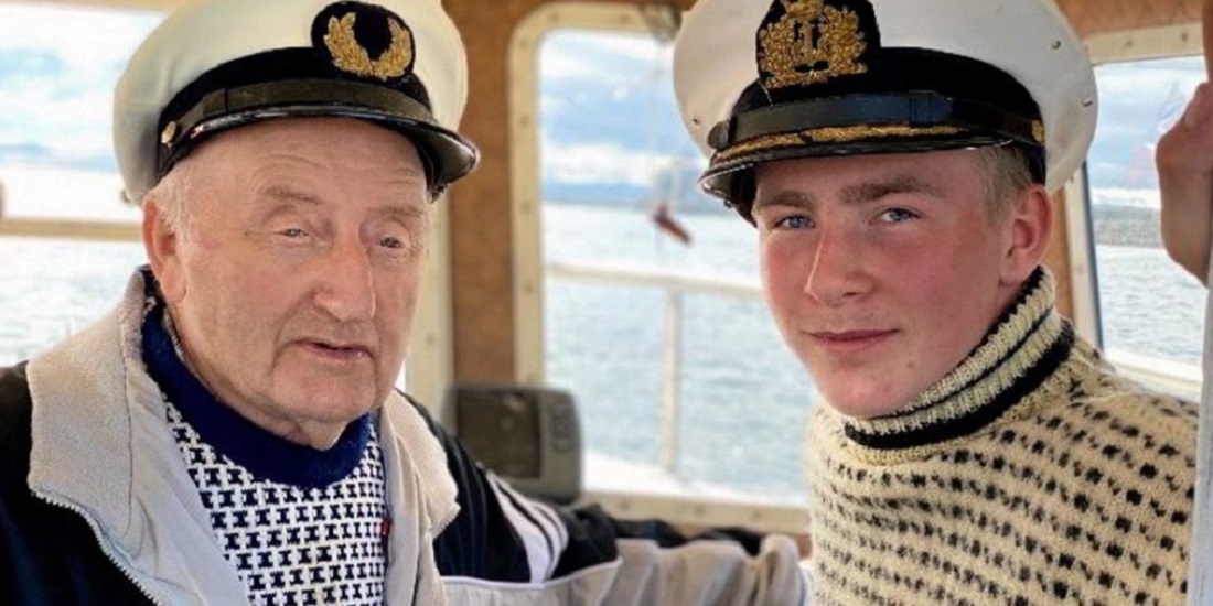 Kystsamfunn. Bildet viser en bestefar og barnebarnet i skipperluer om bord i en båt.