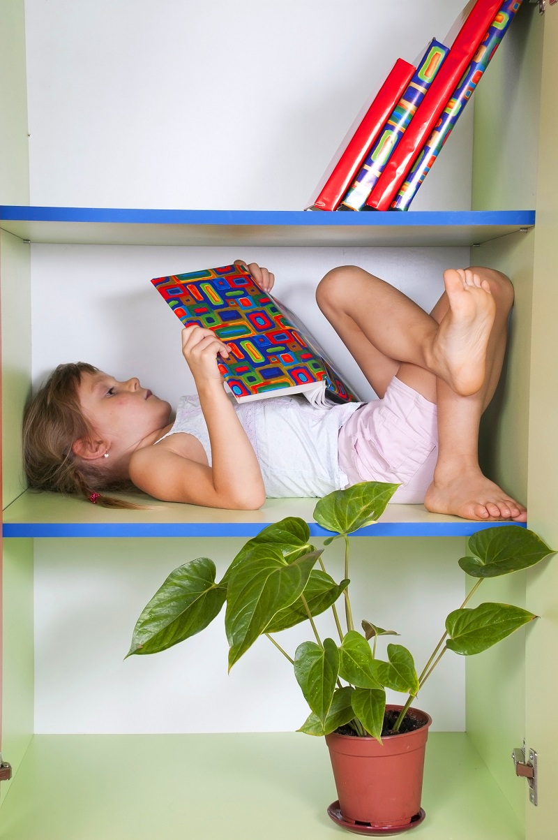 Leseferdigheter. Bildet viser ei jente som ligger i bokhyllen og leser.
