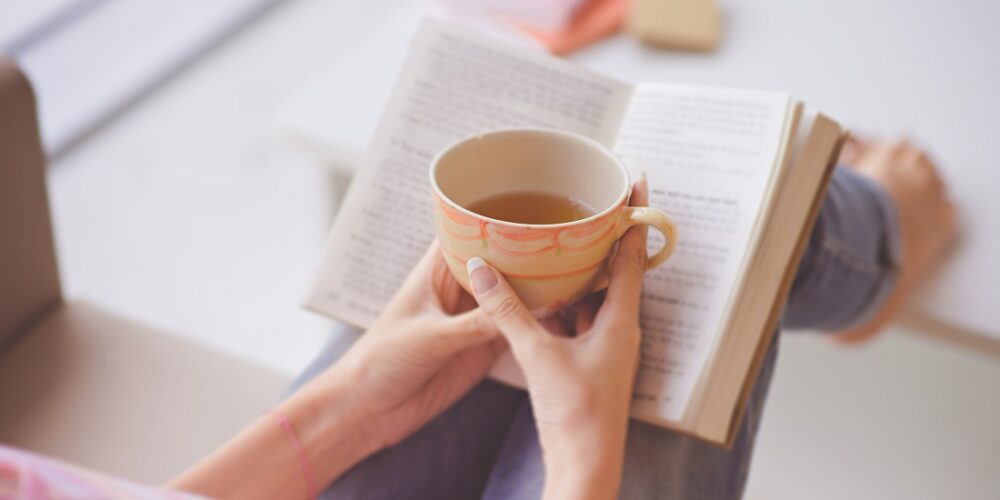 Ordforrådet. Bildet viser to hender som holder rundt en kopp te på en bok.
