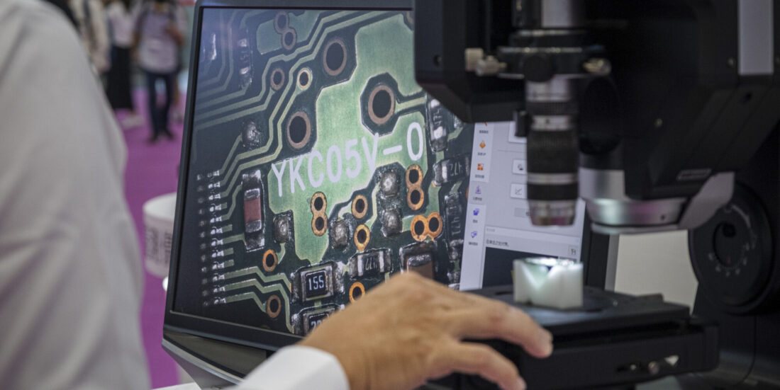 Hånd ses foran dataskjerm med oppblåst bilde av mikrobrikker