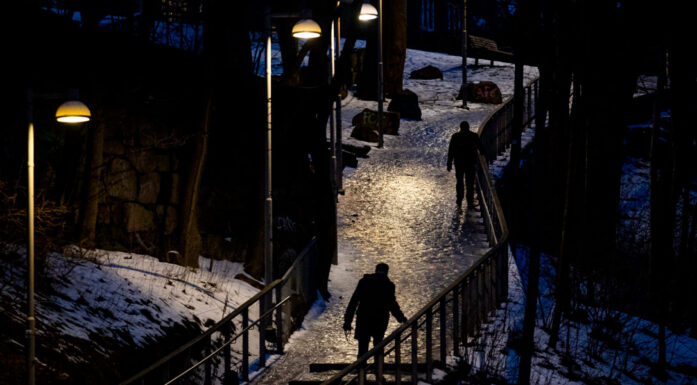 Kveldsbilde viser silhuetter av to mennesker som går på sti med hålke i skinnet fra gatelykter.