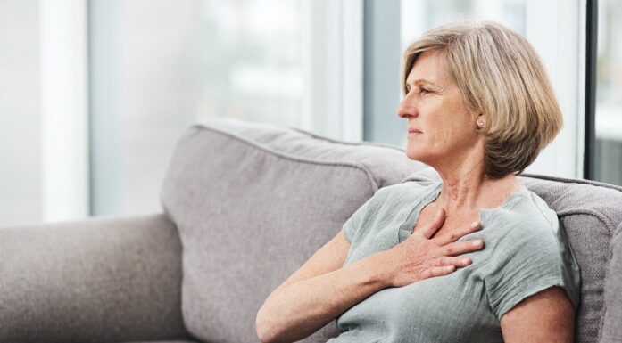 Kolesterol. Bildet viser en kvinne som tar seg til brystet mens hun sitter i en sofa.