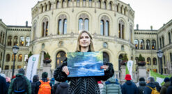 Kvinne står foran Stortinget med bildet av en urørt elv. Bak henne ses flere demonstranter.