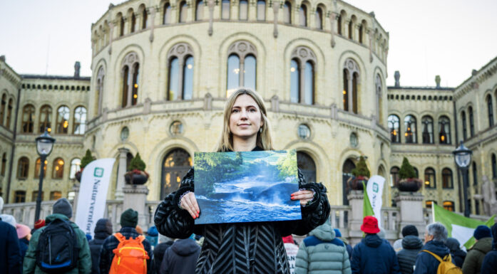 Kvinne står foran Stortinget med bildet av en urørt elv. Bak henne ses flere demonstranter.