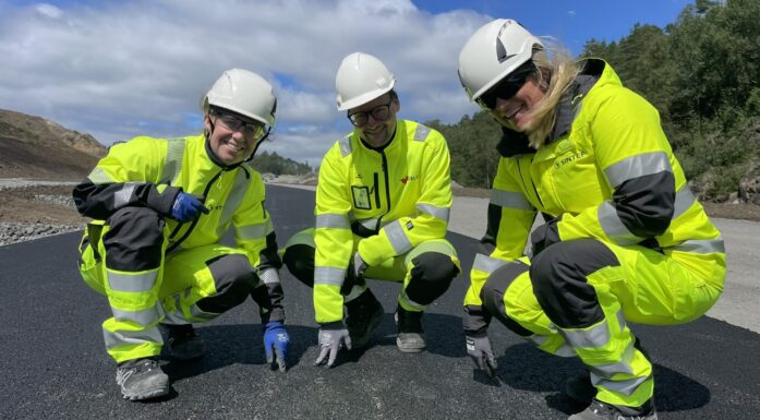 Tre personer i gule arbeidsdresser viser fram ny asfalt - som er basert på gjenbruksmaterialer.