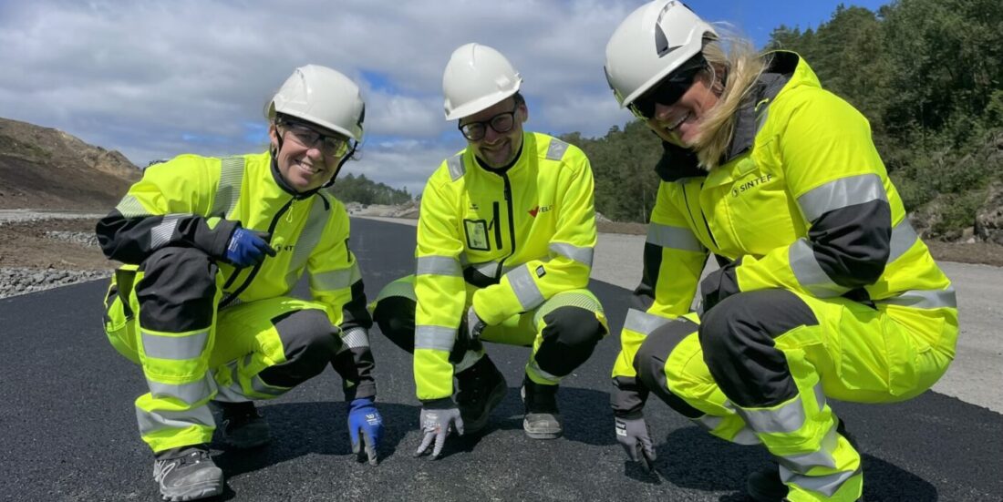 Tre personer i gule arbeidsdresser viser fram ny asfalt - som er basert på gjenbruksmaterialer.
