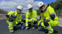 Tre personer i gule arbeidsdresser viser fram ny asfalt - som er basert på gjenbruksmaterialer.