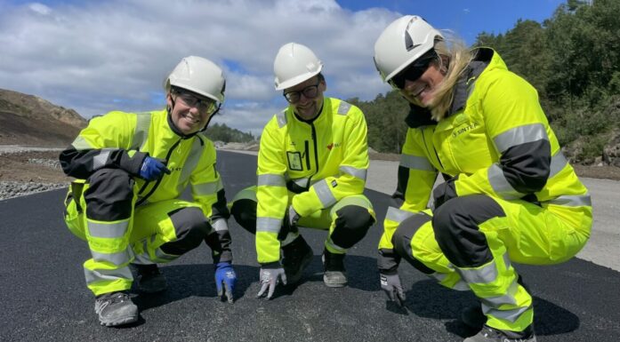Tre personer i gule arbeidsdresser viser fram ny asfalt - som er basert på gjenbruksmaterialer.