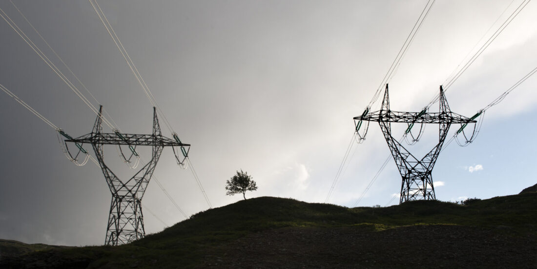 To kraftmaster ruver mot skyet himmel, med et bittelite tre mellom seg.