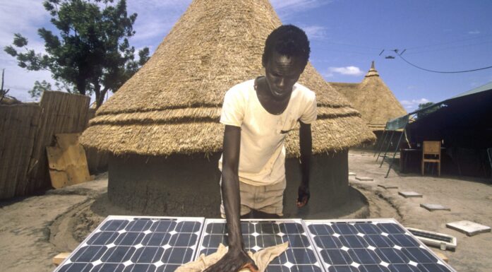 Gutt pusser på solcellepanel foran afrikansk landsbyhus.