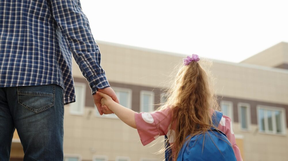 Grunnskolen. Bildet viser ei skolejente som holder en voksen i hånden.