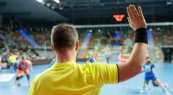 Håndballdommere. Bildet viser en håndballdommer bakfra med den ene hånda i været.