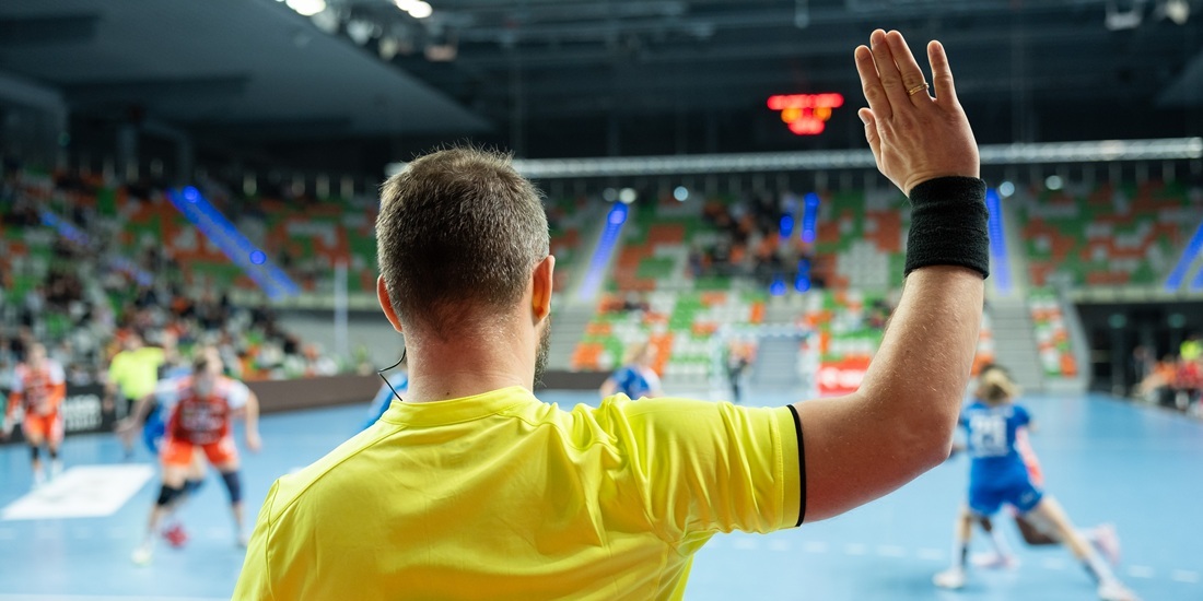 Håndballdommere. Bildet viser en håndballdommer bakfra med den ene hånda i været.